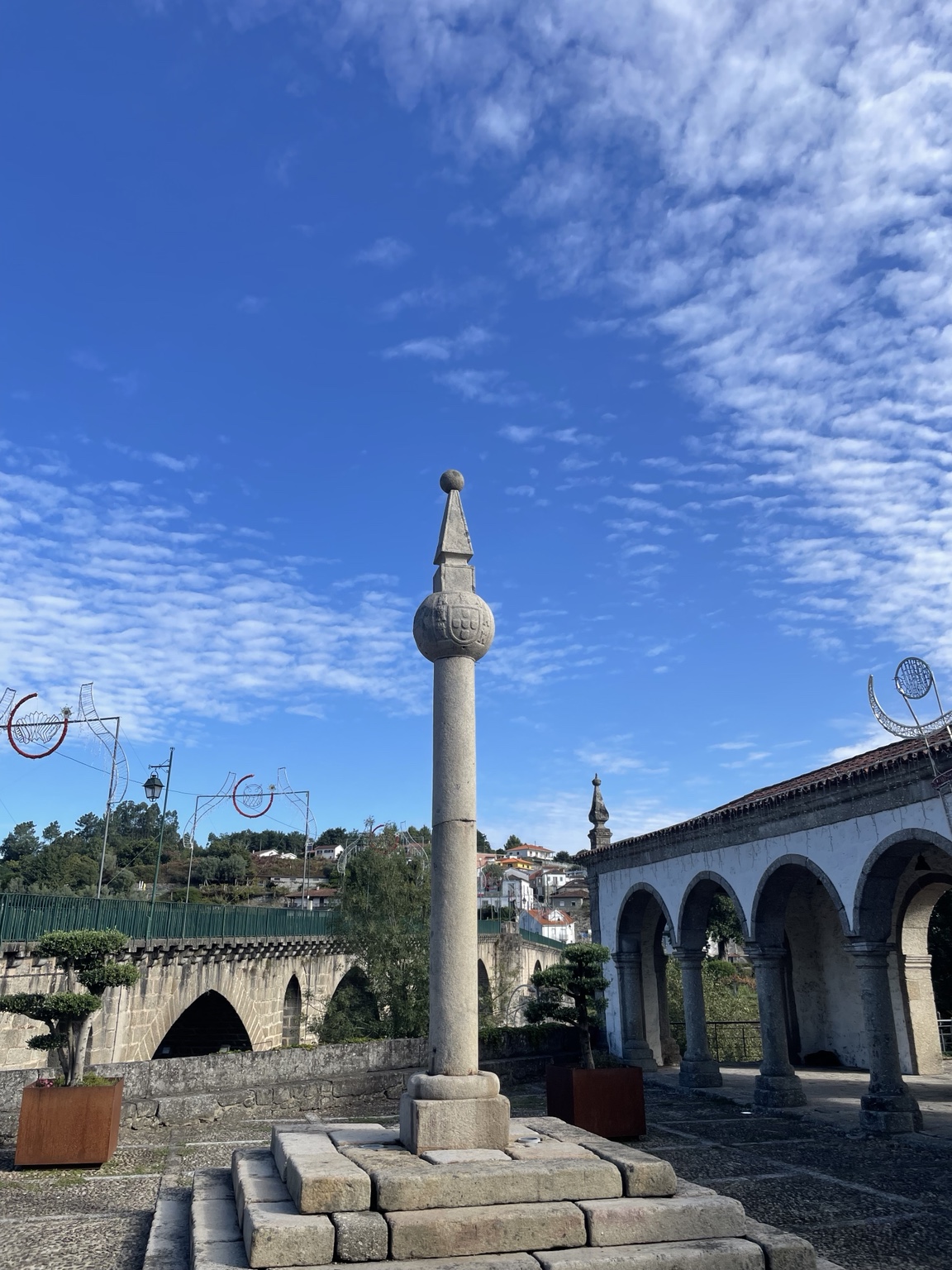 Pelourinho com o brasão de Portugal junto às arcadas e à ponte, em Ponte da Barca
