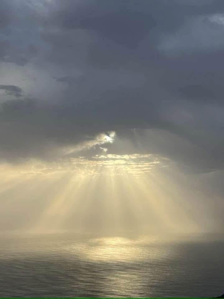 Raios de sol atravessam as nuvens e iluminam o mar visto do alto da Peninha